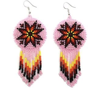 A pair of handmade beaded earrings featuring a circular design. The earrings have a starburst pattern in the center with black, red, orange, and yellow beads, set against a pink background. Below the circle, beaded fringe extends in a triangular shape, incorporating yellow, orange, red, and black beads. The earrings are attached to metal fishhook-style ear wires for wearing.